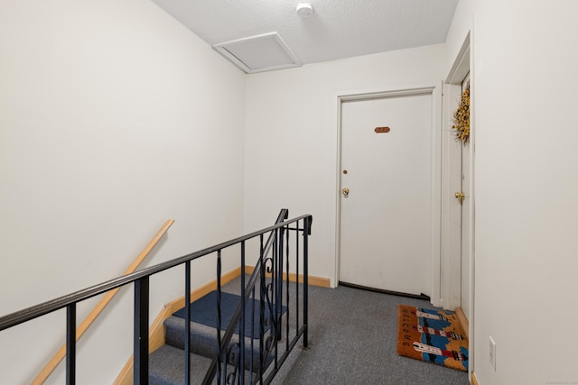 staircase featuring a textured ceiling, carpet, attic access, and baseboards