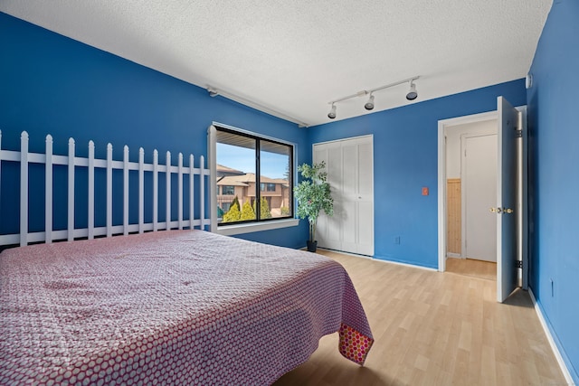 bedroom featuring light wood-type flooring, a closet, baseboards, and a textured ceiling