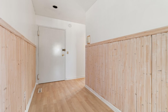 hallway featuring wooden walls, visible vents, and light wood-style floors