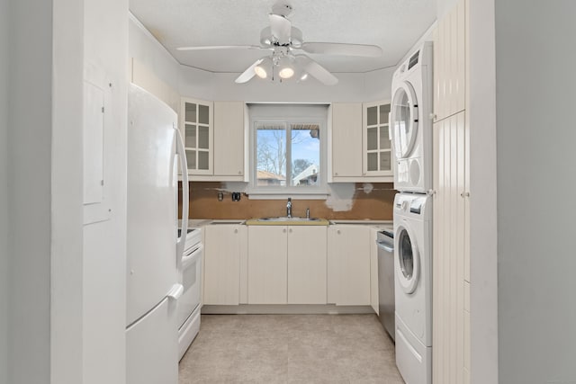 kitchen featuring white appliances, glass insert cabinets, a sink, and stacked washer and clothes dryer