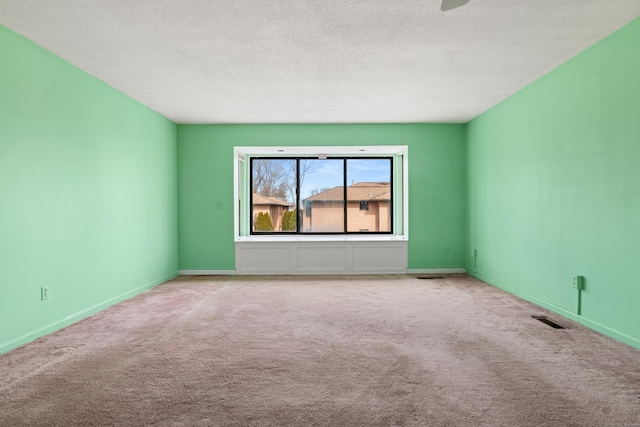 carpeted spare room featuring a textured ceiling, visible vents, and baseboards