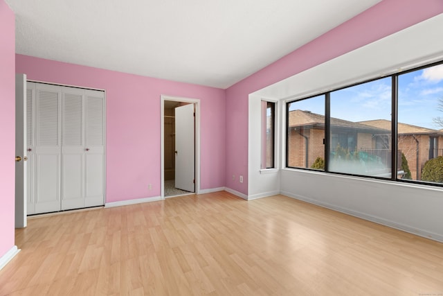 unfurnished bedroom featuring a closet, light wood-style flooring, baseboards, and ensuite bathroom