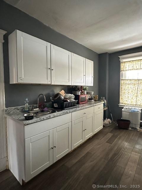 kitchen with dark wood-style floors, light stone counters, a sink, and white cabinets