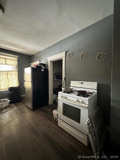 kitchen with dark wood-style floors, light countertops, white gas range oven, and freestanding refrigerator