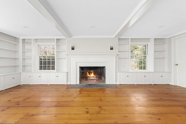 unfurnished living room featuring built in shelves, wood-type flooring, a fireplace, and crown molding