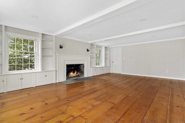 unfurnished living room with built in shelves, baseboards, a brick fireplace, beam ceiling, and hardwood / wood-style floors