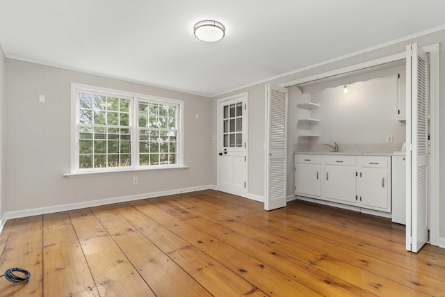 unfurnished dining area featuring baseboards, ornamental molding, a sink, and light wood-style floors