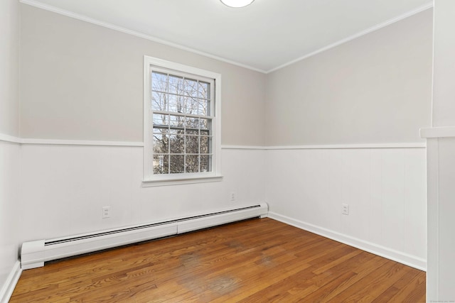 empty room with a baseboard heating unit, a wainscoted wall, ornamental molding, and wood finished floors