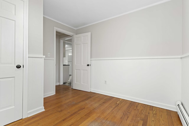 unfurnished bedroom with a wainscoted wall, crown molding, baseboard heating, and hardwood / wood-style flooring