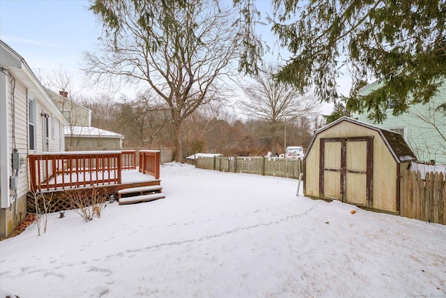 yard layered in snow featuring an outbuilding, fence, a deck, and a shed