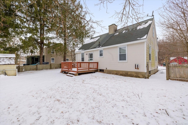 snow covered back of property featuring a chimney, fence, and a deck