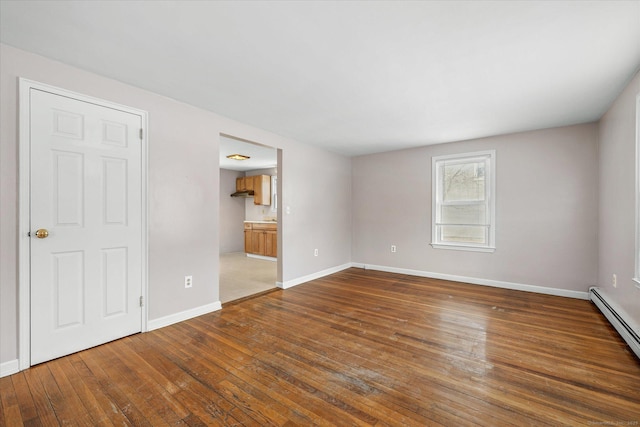 unfurnished room with a baseboard radiator, baseboards, and wood finished floors