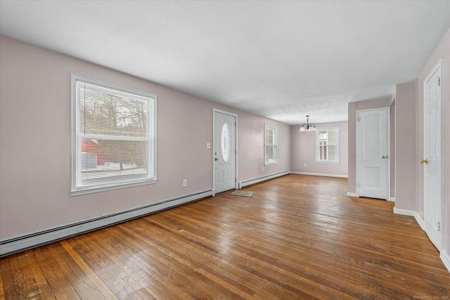 unfurnished living room with an inviting chandelier, a baseboard radiator, baseboards, and wood finished floors