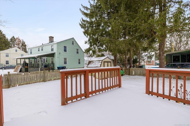 snow covered deck featuring an outbuilding, a storage shed, and fence private yard