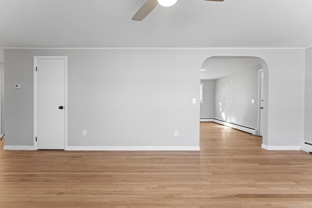 spare room featuring arched walkways, light wood finished floors, a baseboard radiator, ceiling fan, and baseboards