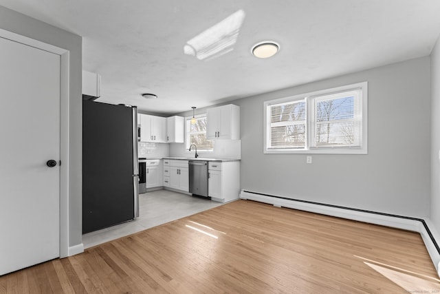 kitchen with stainless steel appliances, light countertops, hanging light fixtures, white cabinetry, and a sink