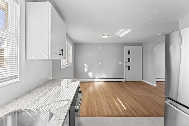 kitchen with arched walkways, a baseboard radiator, white cabinetry, freestanding refrigerator, and light stone countertops