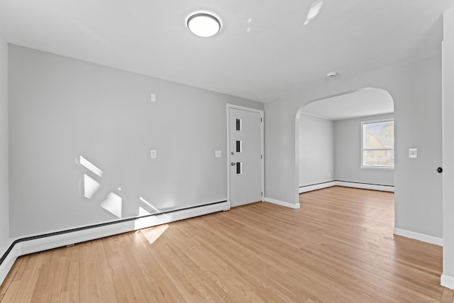 empty room with arched walkways, a baseboard radiator, baseboard heating, light wood-type flooring, and baseboards