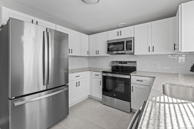 kitchen featuring stainless steel appliances, white cabinets, a sink, and light stone countertops