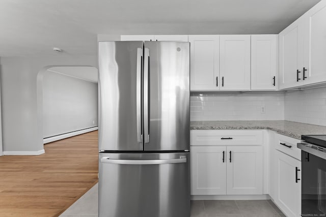 kitchen featuring light stone counters, baseboard heating, freestanding refrigerator, and white cabinetry