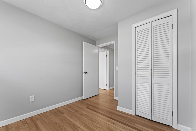 unfurnished bedroom featuring light wood finished floors, a closet, and baseboards