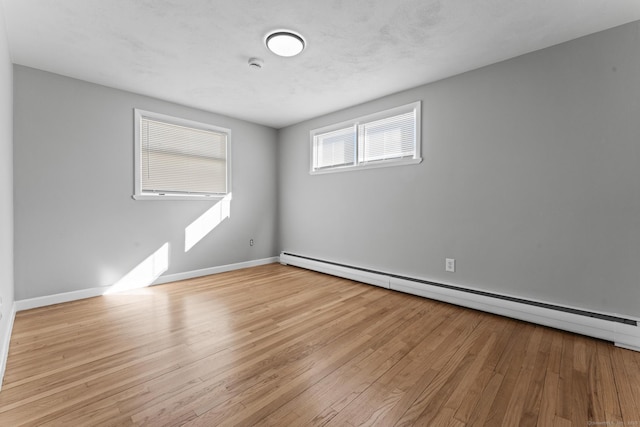 empty room with light wood finished floors, a baseboard radiator, and baseboards