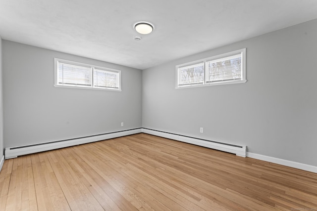 empty room featuring light wood finished floors, baseboard heating, and baseboards