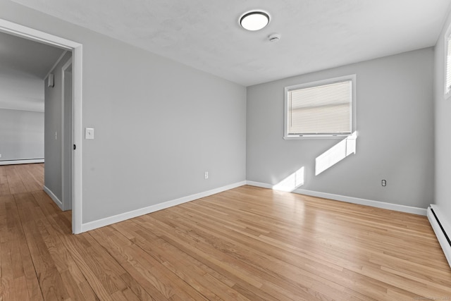 spare room featuring light wood finished floors, a baseboard radiator, and baseboards