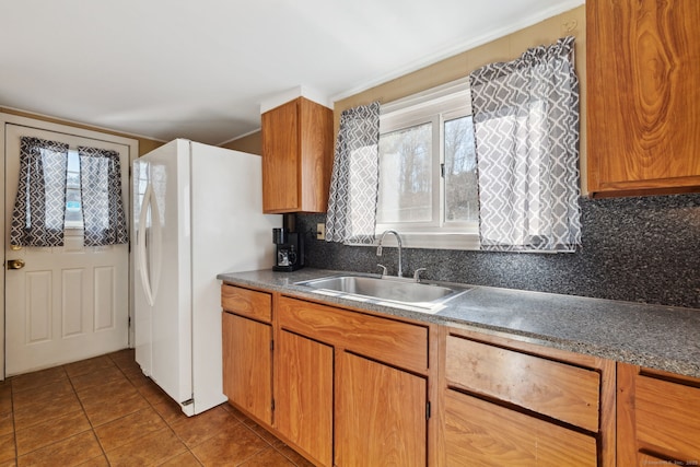 kitchen featuring decorative backsplash, brown cabinetry, freestanding refrigerator, a sink, and tile patterned flooring