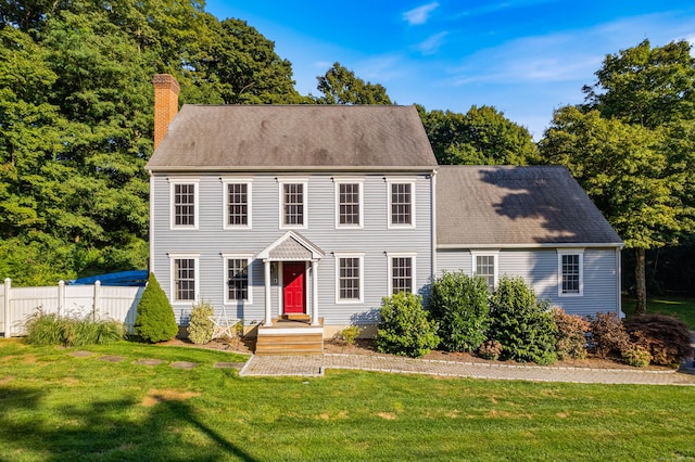 colonial-style house with a shingled roof, a front yard, fence, and a chimney