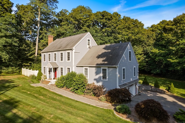 view of front of home with a garage, a chimney, aphalt driveway, roof with shingles, and a front yard