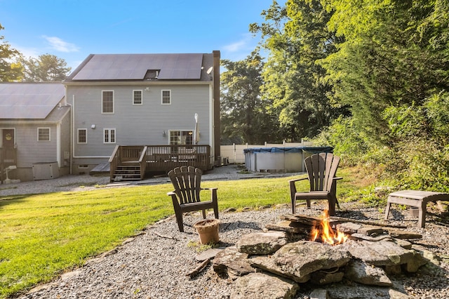 rear view of property with an outdoor fire pit, a wooden deck, solar panels, a covered pool, and a yard