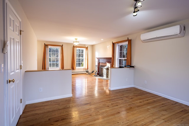 spare room featuring light wood-style floors, a fireplace, baseboards, and an AC wall unit