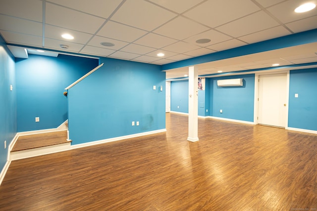 finished below grade area featuring an AC wall unit, stairway, wood finished floors, and baseboards