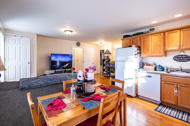 kitchen featuring white appliances, brown cabinets, a sink, and light wood-style flooring