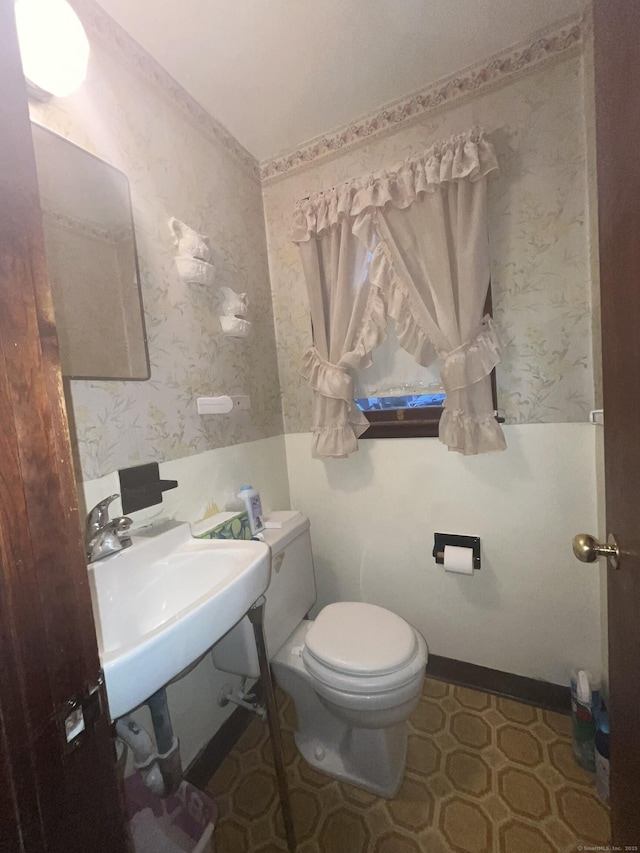 bathroom featuring a sink, baseboards, toilet, and wallpapered walls