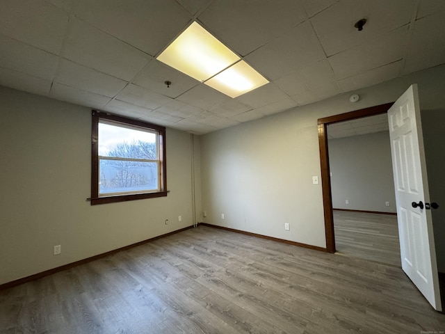 unfurnished room featuring a drop ceiling, light wood-type flooring, and baseboards