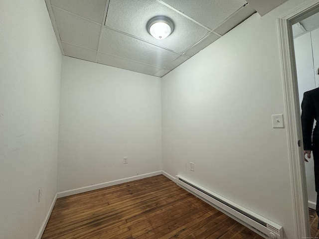 unfurnished room featuring dark wood-type flooring, baseboard heating, a drop ceiling, and baseboards