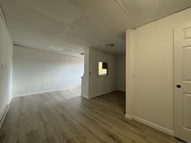 unfurnished room featuring a baseboard heating unit, baseboards, a drop ceiling, and wood finished floors