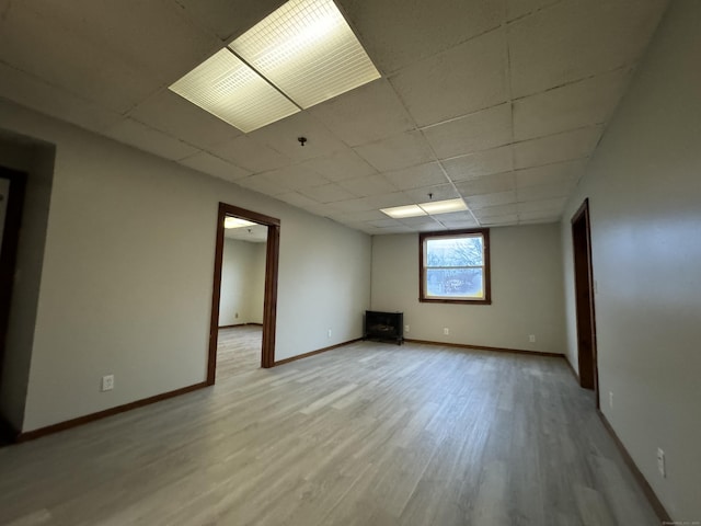 spare room with a paneled ceiling, light wood finished floors, and baseboards