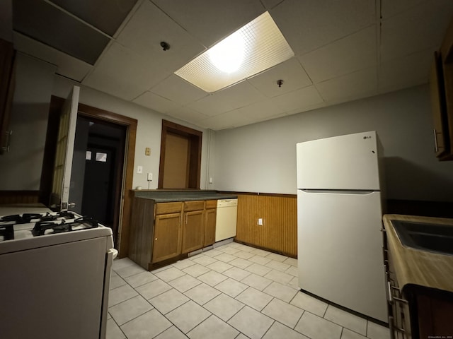 kitchen featuring a wainscoted wall, dark countertops, brown cabinetry, wooden walls, and white appliances