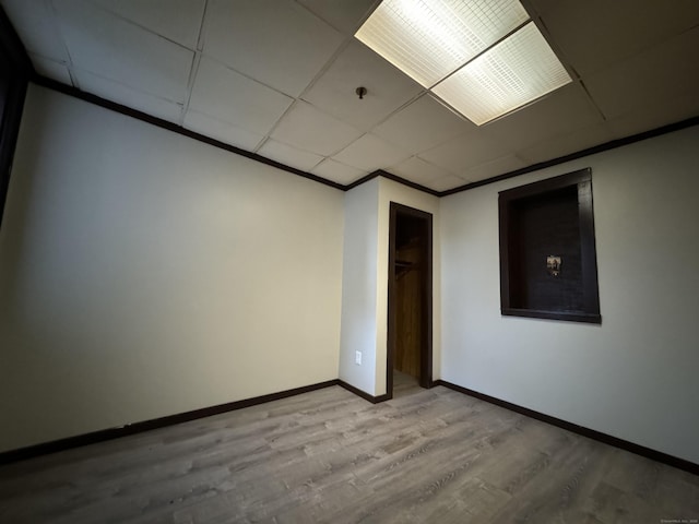 empty room featuring ornamental molding, light wood finished floors, a drop ceiling, and baseboards