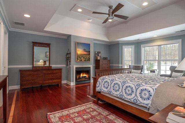 bedroom with a warm lit fireplace, a tray ceiling, visible vents, and wood finished floors