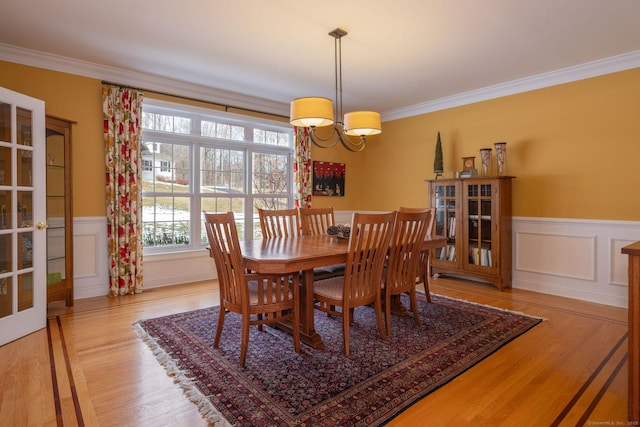 dining room featuring ornamental molding, wainscoting, an inviting chandelier, and wood finished floors