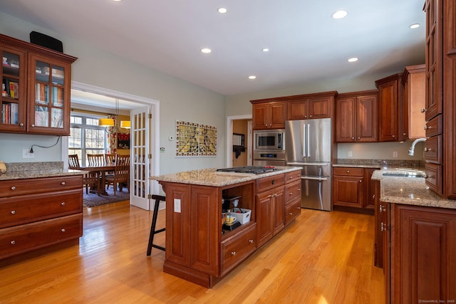 kitchen with brown cabinets, a breakfast bar area, appliances with stainless steel finishes, a sink, and light wood-type flooring