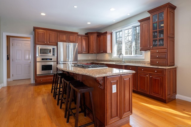 kitchen featuring stainless steel appliances, a sink, a kitchen breakfast bar, a center island, and light wood finished floors