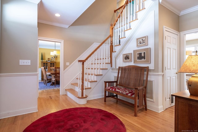 entryway with stairs, light wood finished floors, and crown molding