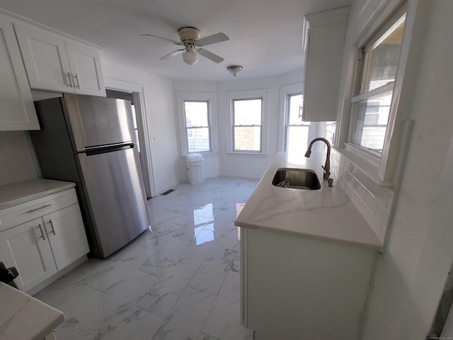 kitchen featuring marble finish floor, a ceiling fan, freestanding refrigerator, white cabinetry, and a sink