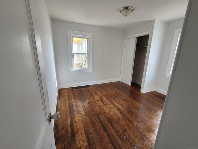 unfurnished bedroom with a closet, visible vents, dark wood finished floors, and baseboards