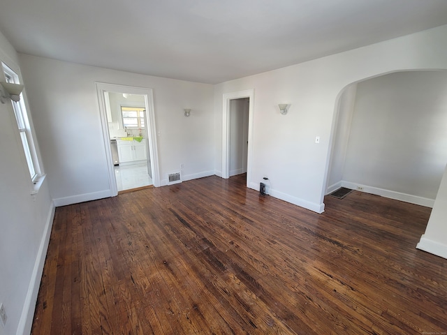 spare room with dark wood-style floors, baseboards, visible vents, and arched walkways